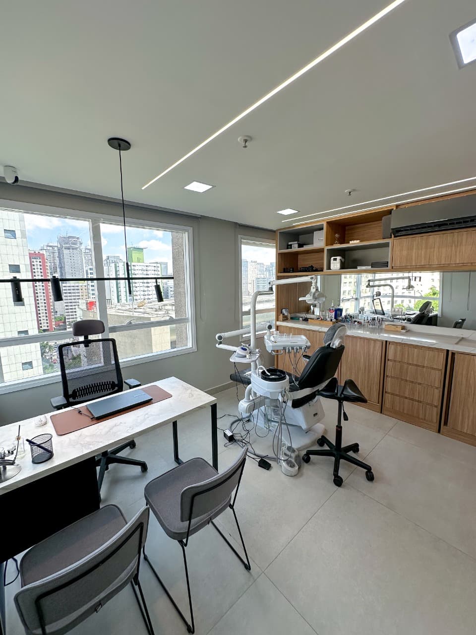 Vista ampla do consultório — equipamento odontológico moderno, marcenaria em madeira e janelas com luz natural